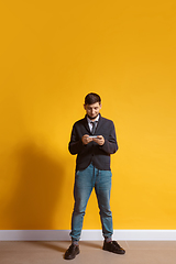 Image showing Young caucasian man using smartphone. Full body length portrait isolated over yellow background.