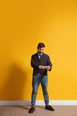 Image showing Young caucasian man using smartphone. Full body length portrait isolated over yellow background.