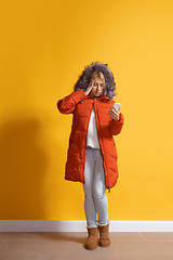 Image showing Young caucasian woman using smartphone. Full body length portrait isolated over yellow background.