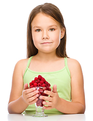 Image showing Happy little girl is eating raspberries