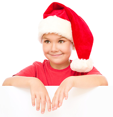 Image showing Little girl in santa hat is holding blank board