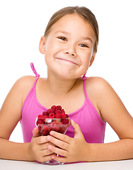 Image showing Happy little girl is eating raspberries