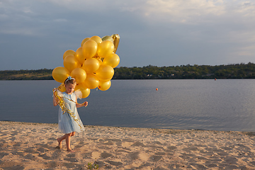 Image showing Little girl with many golden balloons on the beach at sunset