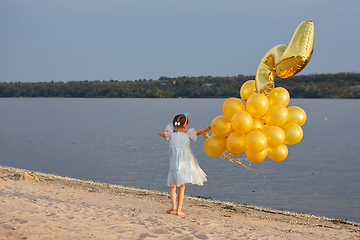 Image showing Little girl with many golden balloons on the beach at sunset