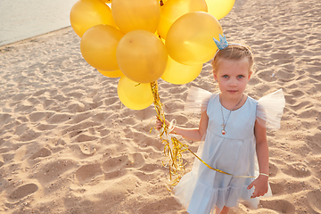 Image showing Little girl with many golden balloons on the beach at sunset