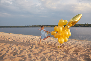 Image showing Little girl with many golden balloons on the beach at sunset
