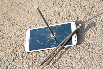 Image showing metal nail and smartphone with a broken screen over the stone surface. The concept of strength.