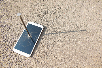 Image showing metal nail and smartphone with a broken screen over the stone surface. The concept of strength.