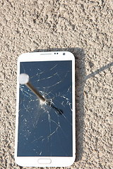 Image showing metal nail and smartphone with a broken screen over the stone surface. The concept of strength.