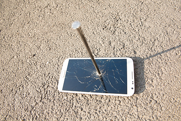 Image showing metal nail and smartphone with a broken screen over the stone surface. The concept of strength.