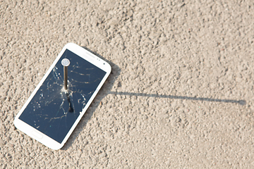 Image showing metal nail and smartphone with a broken screen over the stone surface. The concept of strength.