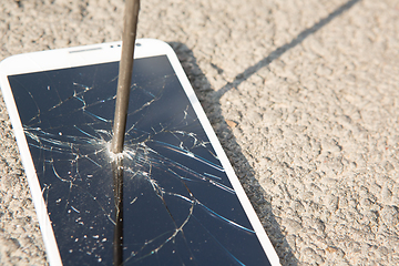 Image showing metal nail and smartphone with a broken screen over the stone surface. The concept of strength.