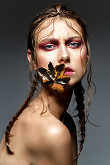 Image showing beautiful girl with modern braids and metal flower in mouth