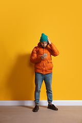 Image showing Young caucasian man using smartphone. Full body length portrait isolated over yellow background.