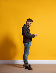 Image showing Young caucasian man using smartphone. Full body length portrait isolated over yellow background.