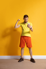 Image showing Young caucasian man using smartphone. Full body length portrait isolated over yellow background.