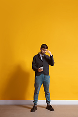 Image showing Young caucasian man using smartphone. Full body length portrait isolated over yellow background.