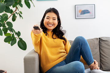 Image showing asian woman with tv remote sitting on sofa at home