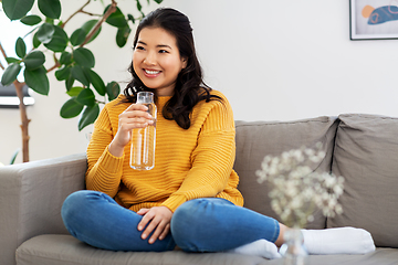 Image showing smiling asian young woman drinking water at home