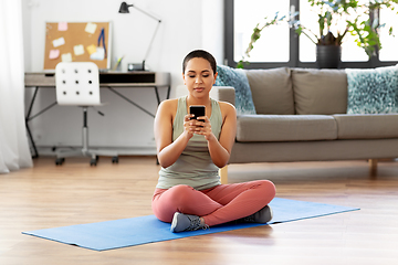 Image showing woman with smartphone sits on exercise mat at home