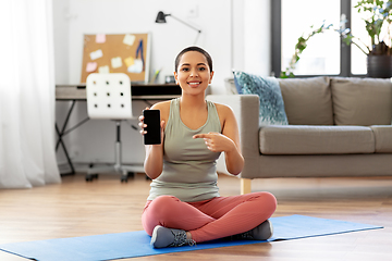 Image showing woman with smartphone sits on exercise mat at home