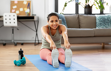 Image showing african woman with earphones stretching at home