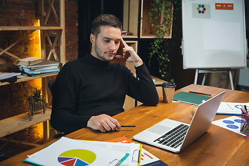 Image showing Young man working in modern office using devices and gadgets. Making reports, analitycs, routine processing tasks