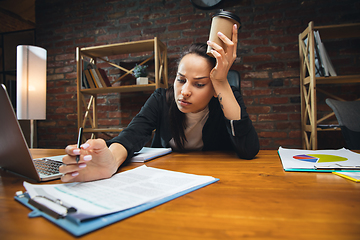 Image showing Young woman working in modern office using devices and gadgets. Making reports, analitycs, routine processing tasks