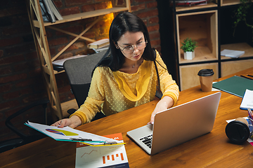 Image showing Young woman working in modern office using devices and gadgets. Making reports, analitycs, routine processing tasks