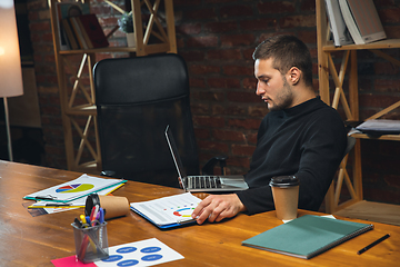 Image showing Young man working in modern office using devices and gadgets. Making reports, analitycs, routine processing tasks