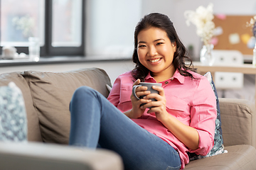 Image showing smiling asian young woman drinking coffee at home