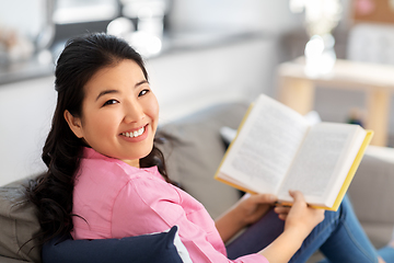 Image showing smiling asian young woman reading book at home