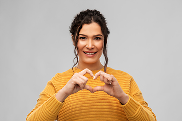 Image showing smiling young woman making hand heart gesture