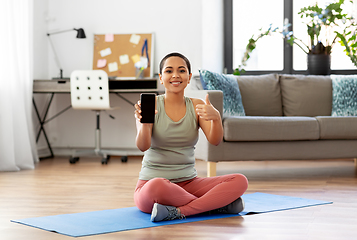 Image showing woman with smartphone sits on exercise mat at home
