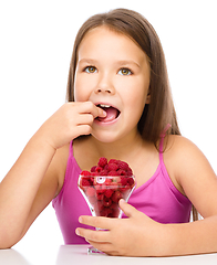 Image showing Happy little girl is eating raspberries