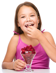 Image showing Happy little girl is eating raspberries