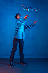 Image showing Caucasian young skateboarder posing on dark neon lighted background