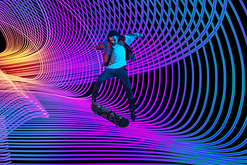 Image showing Caucasian young skateboarder riding on dark neon lighted line background