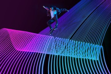 Image showing Caucasian young skateboarder riding on dark neon lighted line background