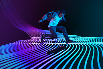 Image showing Caucasian young skateboarder riding on dark neon lighted line background