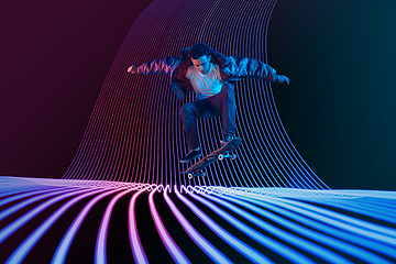 Image showing Caucasian young skateboarder riding on dark neon lighted line background