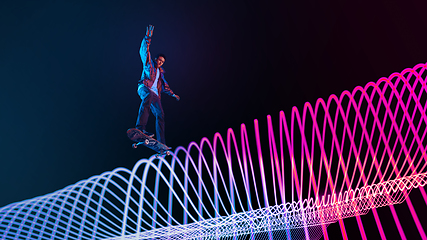 Image showing Caucasian young skateboarder riding on dark neon lighted line background