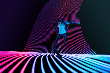 Image showing Caucasian young skateboarder riding on dark neon lighted line background