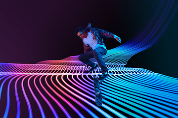 Image showing Caucasian young skateboarder riding on dark neon lighted line background