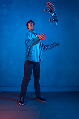 Image showing Caucasian young skateboarder posing on dark neon lighted background