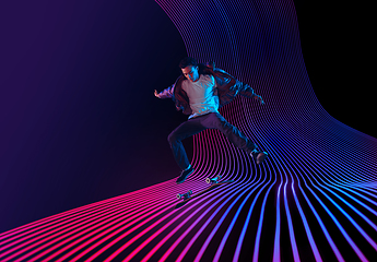 Image showing Caucasian young skateboarder riding on dark neon lighted line background