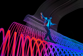 Image showing Caucasian young skateboarder riding on dark neon lighted line background