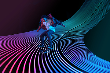 Image showing Caucasian young skateboarder riding on dark neon lighted line background