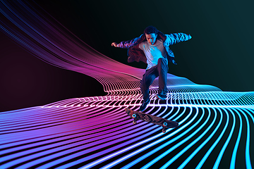 Image showing Caucasian young skateboarder riding on dark neon lighted line background