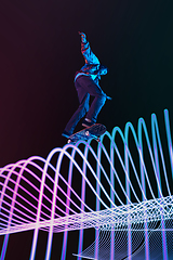 Image showing Caucasian young skateboarder riding on dark neon lighted line background